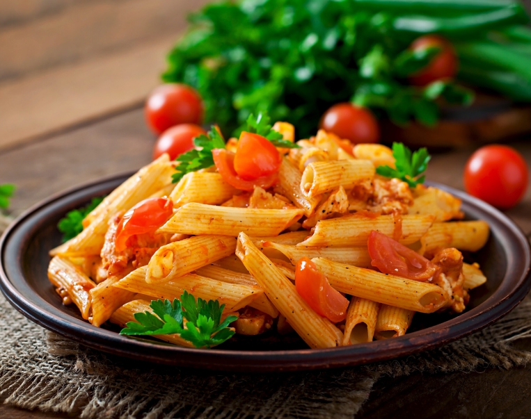 Penne pasta in tomato sauce with chicken and tomatoes  on a wooden table
