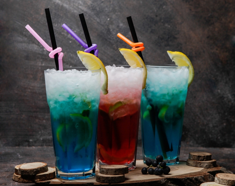 Close-up alcohol cocktails glasses of blue lagoon cocktail decorated with lemon and glass of cocktail with whiskey on a wooden stand